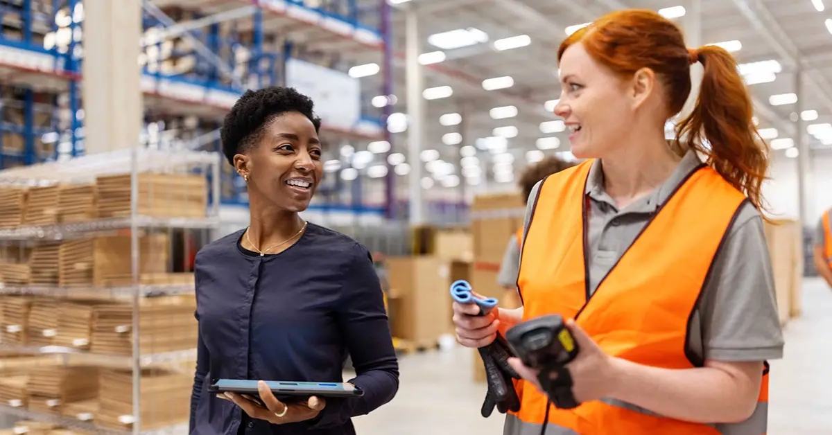 Two female store employees talking as they walk down an aisle.