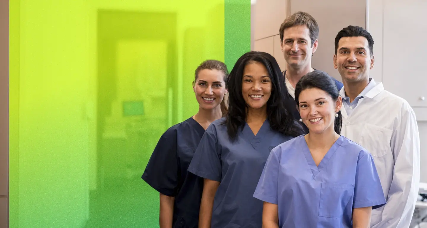 Five smiling healthcare providers in scrubs and a white coat stand together in a bright clinical setting